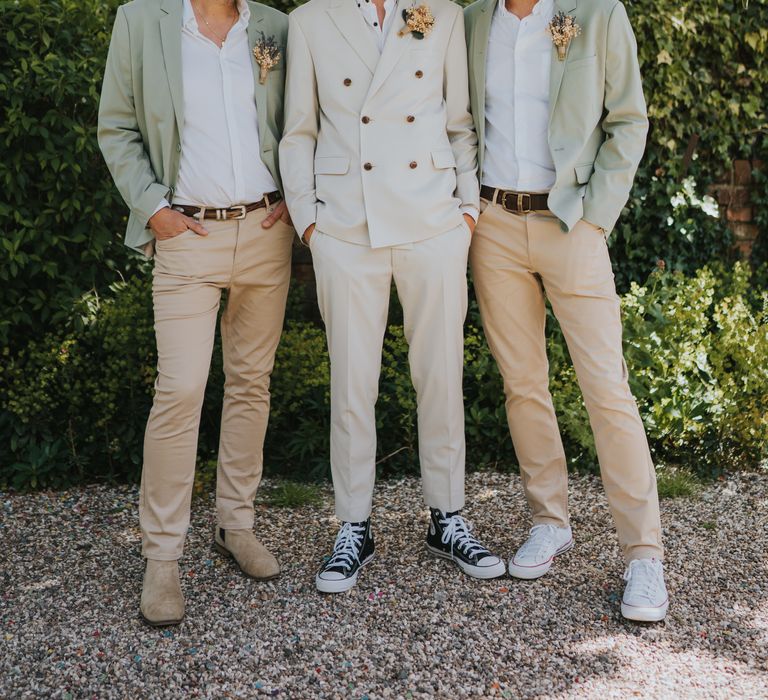 Groom in neutral coloured double-breasted ASOS suit and black high-top converse with dried flower and foliage boutonniere and groomsmen in light chinos, white shirts and sage green blazers 