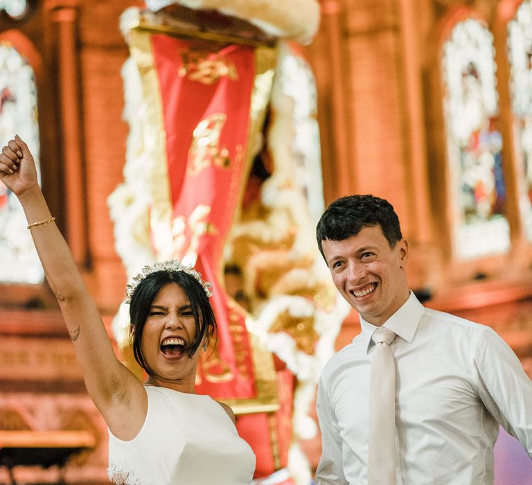 East Asian bride in fitted wedding dress celebrates alongside her groom in off-white white shirt and tie