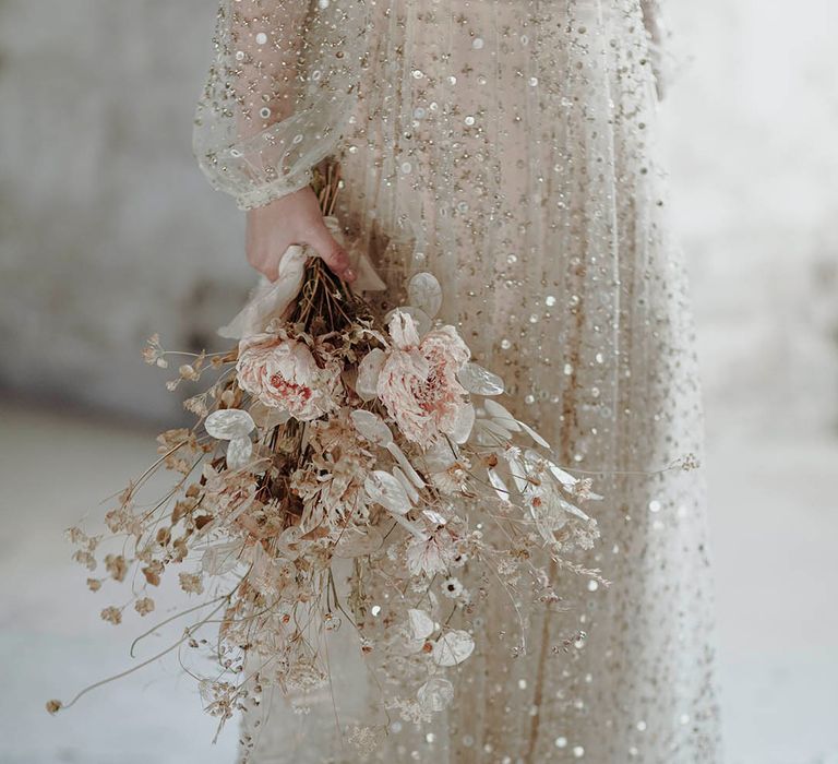 Bride wears sequin embellished wedding dress for alternative bridal outfit whilst carrying dried floral bouquet