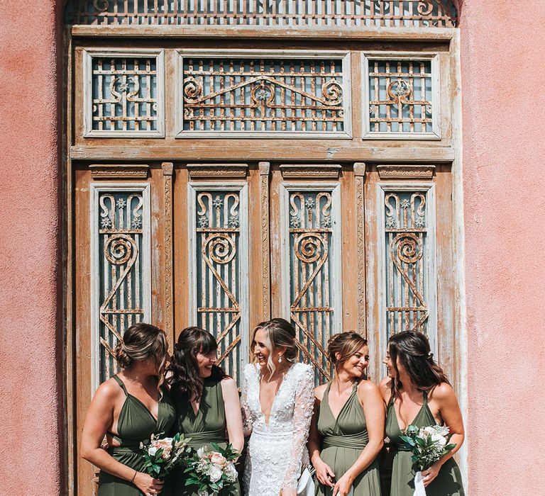 Bridesmaids in dark green bridesmaid dresses with white flower bouquets tied with white ribbon standing with the bride in a 3D lace wedding dress 