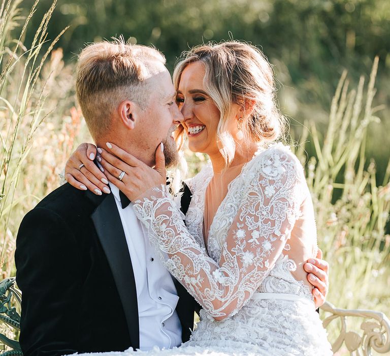 Groom in black tie tuxedo smiling with bride in a sparkly 3D lace wedding dress with long sleeves and shoulder pads 