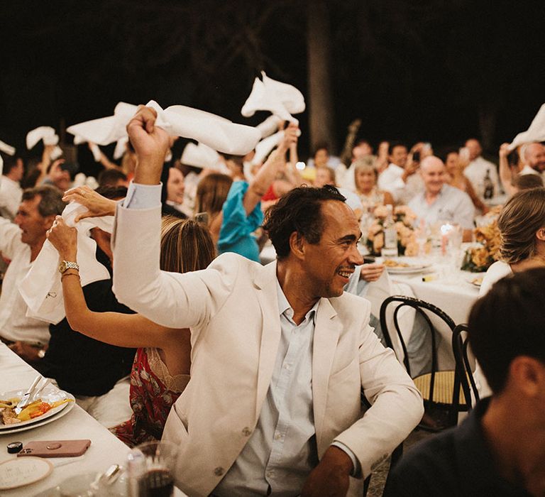 Wedding guests spin napkin in the air during outdoor Tuscan wedding reception