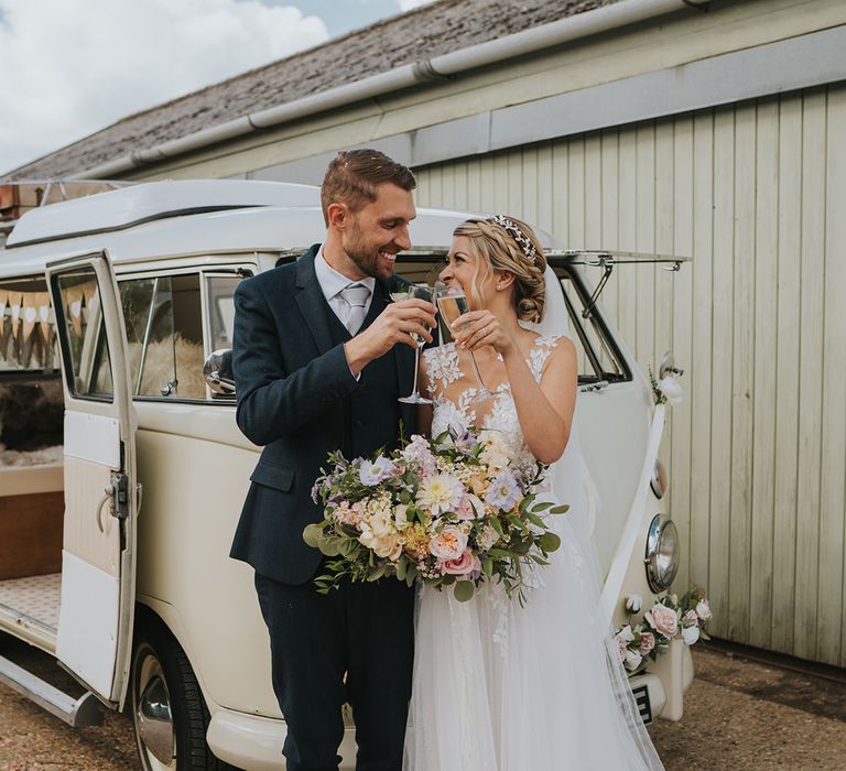 The bride and groom cheers their glasses of champagne in front of their cream VW camper van transport 