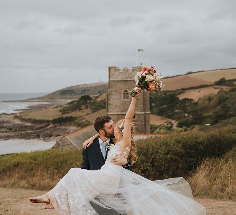 Groom in navy suit with light blue tie lifting and kissing the bride in her Anna Kara tulle wedding dress with a pastel wedding bouquet 