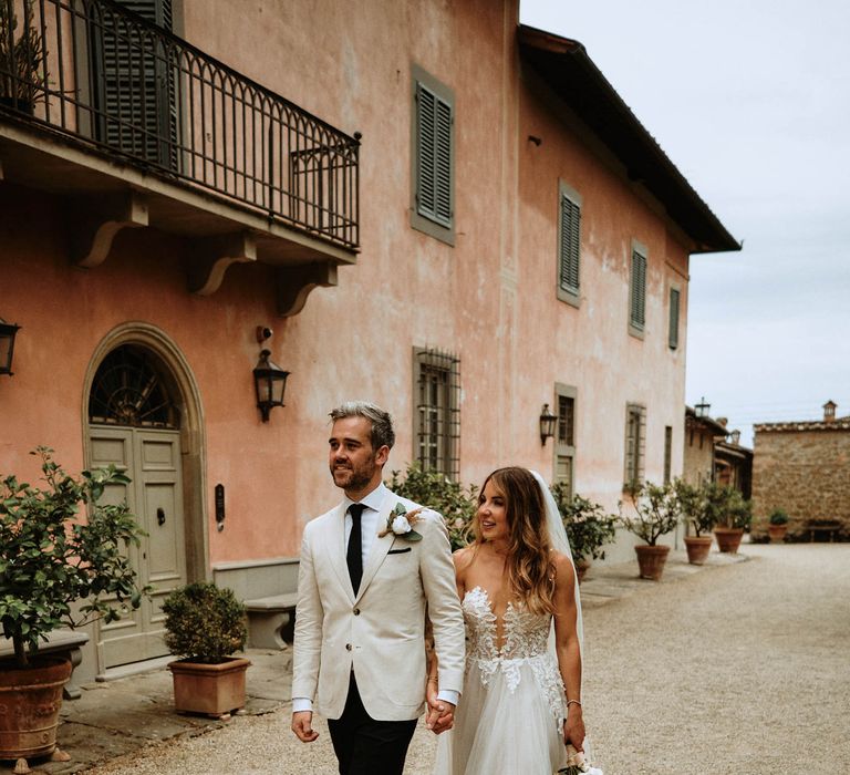 Bride and groom walk hand in hand through italian villa at destination wedding