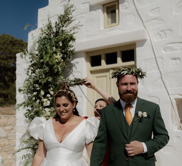 Bride and Groom taking part in the Greek wedding tradition of Stefana crowns during intimate ceremony at white chapel