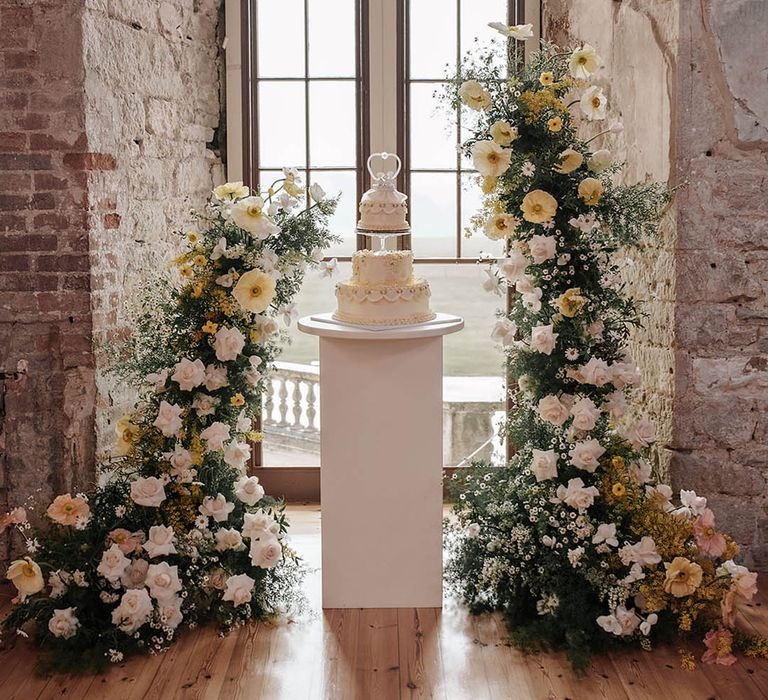 Pastel yellow and white wedding flower columns surround the epic retro wedding cake made by the bride 