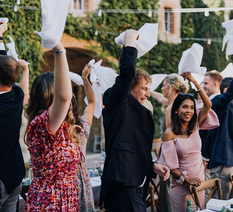 wedding guests waving napkins in the air at an outdoor destination wedding reception 