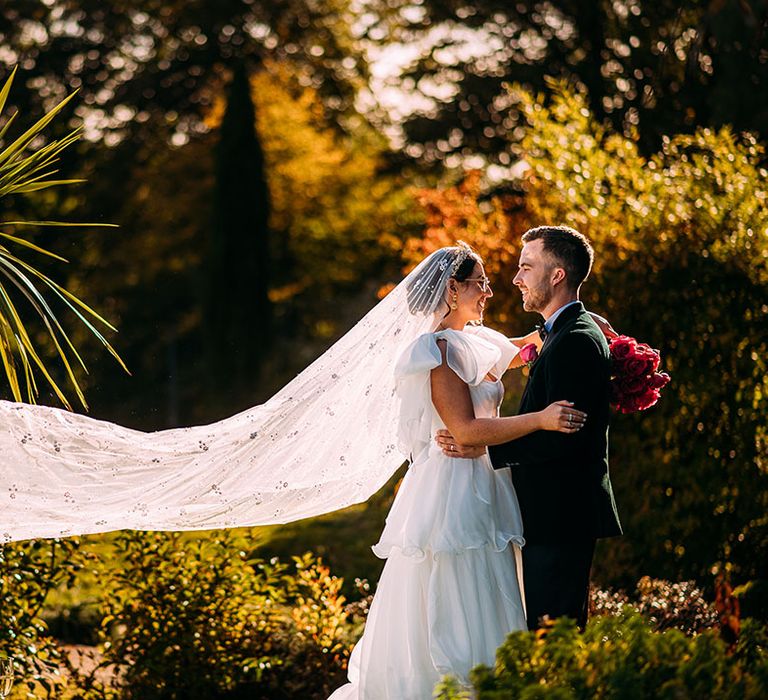 Bride in ruffle Emma Beaumont wedding dress with cathedral length beaded wedding veil with the groom in black tie 