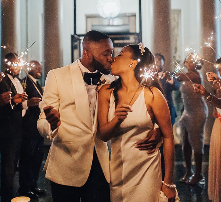 Black bride in slip dress for wedding with the groom at their sparkler send off in the evening 