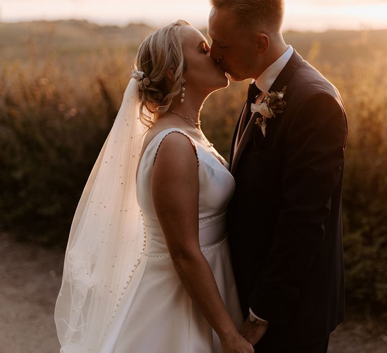 Bride wearing pearl veil with the groom in traditional three piece suit for the golden hour portraits 