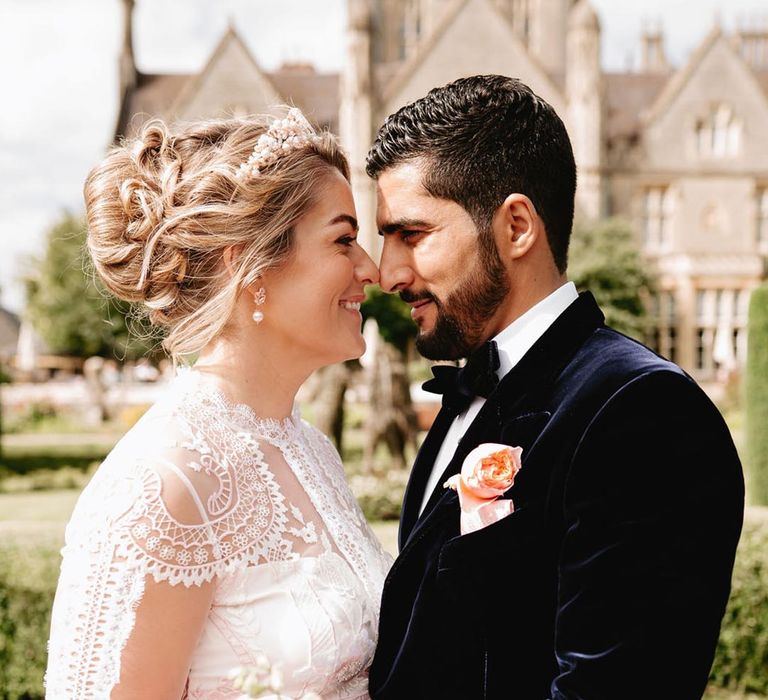 Bride holding pink and white oversized wedding bouquet in long sleeve lace wedding dress with the groom in blue velvet tuxedo 