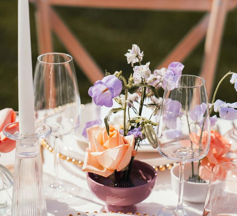 Peach garden rose and lilac sweet pea wedding table centrepieces in small round ceramic pots with gold crockery and tinted glassware 