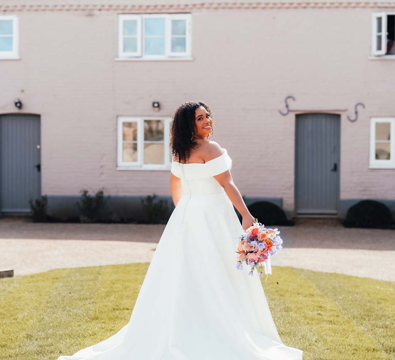 Bride in off shoulder puddle train wedding dress holding orange, lilac and peach mixed flower bridal bouquet at Rackleys Barn