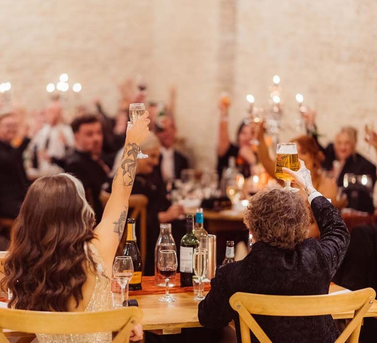 Bride and groom raising a glass to wedding guests during wedding speeches at Kingscote Barn Tetbury wedding venue 