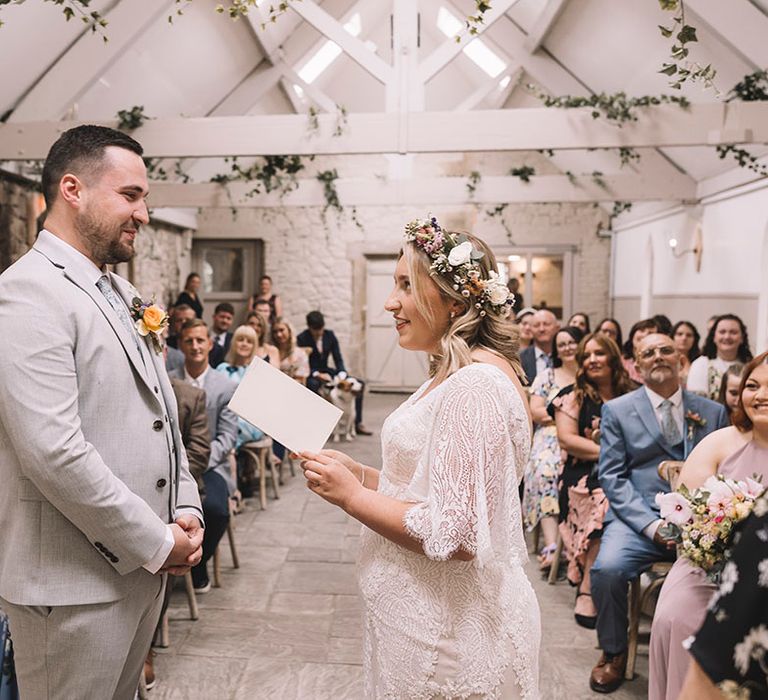 Bride in boho lace wedding dress reading out wedding vows to groom at the altar 