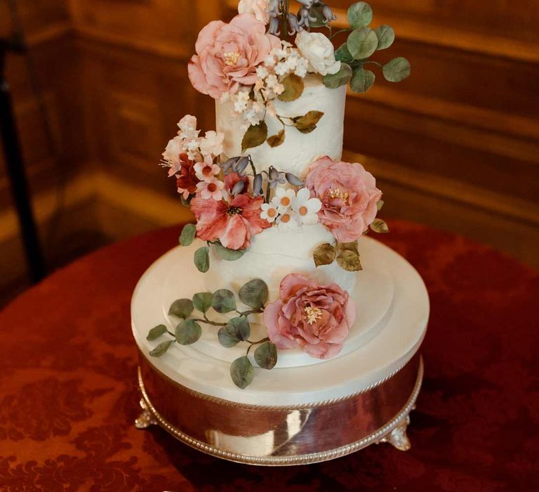 Two tiered buttercream iced wedding cake with decorative floral wedding cake toppers on gold cake stand