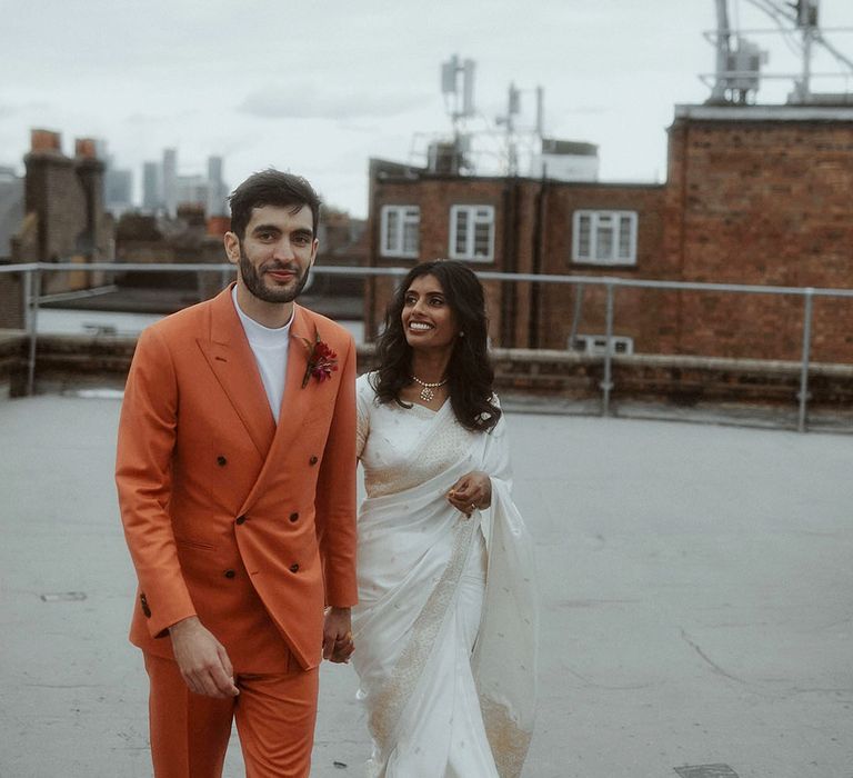 Groom in double breasted orange suit jacket walking with the bride at their city wedding 