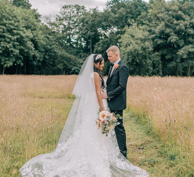 Bride wearing embroidered end wedding veil and floral lace wedding dress with the groom in black tie 