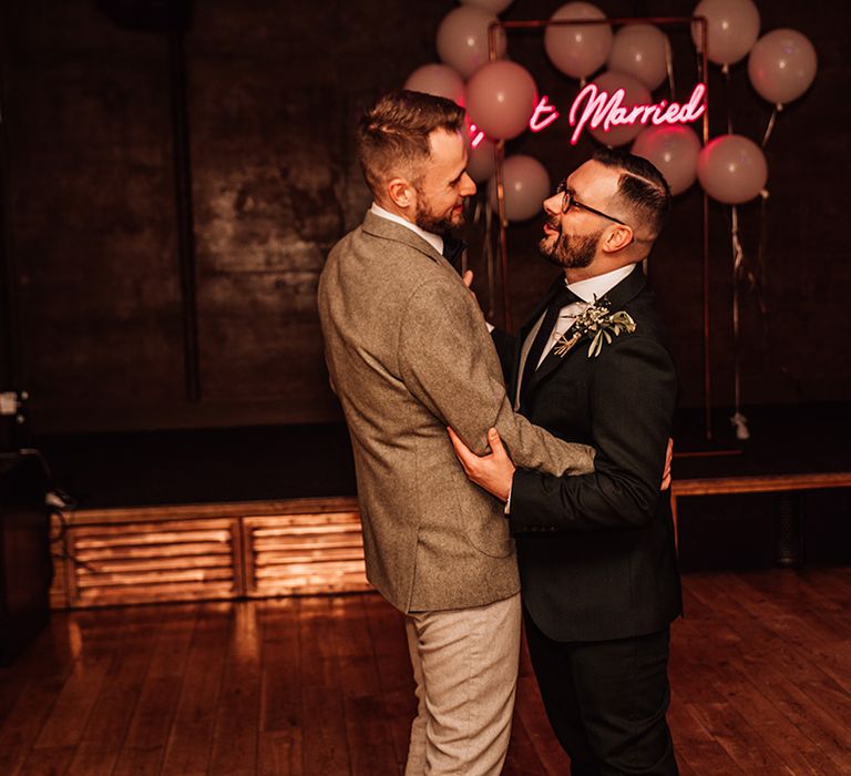 The two groom have their first dance together with pink neon sign wedding decor 