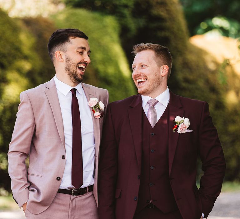 Groom in dusky pink taupe suit with burgundy tie smiling with the best man in a burgundy suit and pink tie 