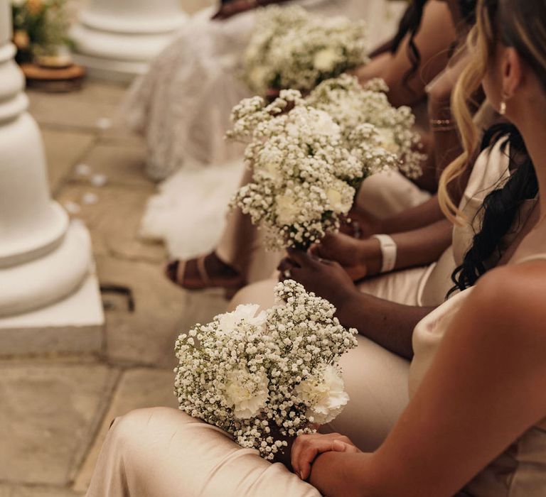 Bridesmaids sit in champagne satin dresses holding bouquets of white gypsophila 