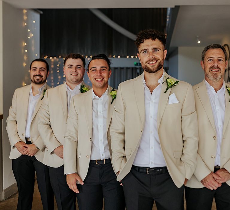 Groom and groomsmen in beige suit jackets with white flower buttonholes 