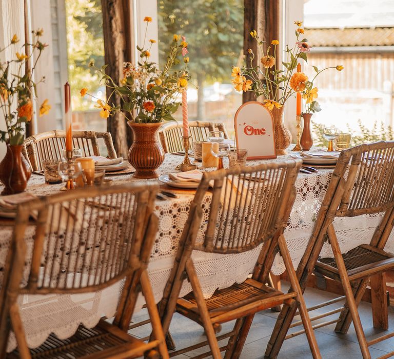 Arched orange and white wedding table number sign with vases full of yellow and orange flowers 