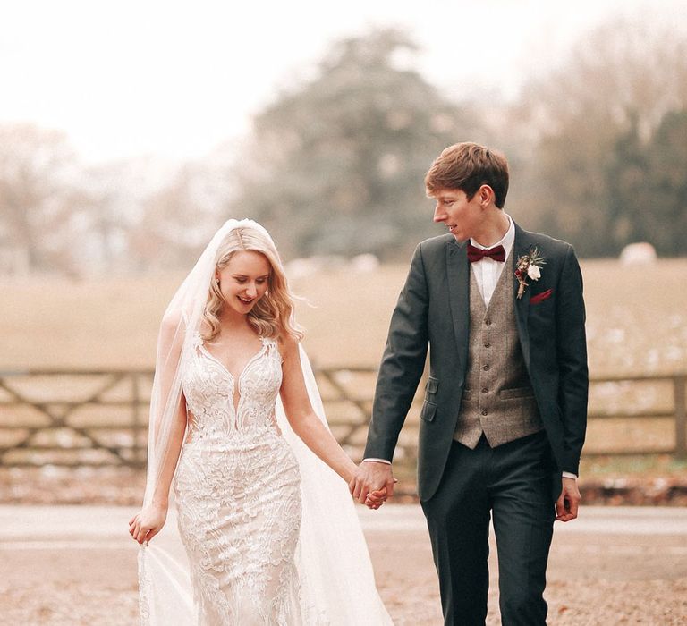 Groom in navy three piece and red bow tie with bride in embellished lace wedding dress 