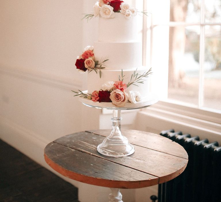 Three tier white iced wedding cake decorated with red, pink, and white rose decor 