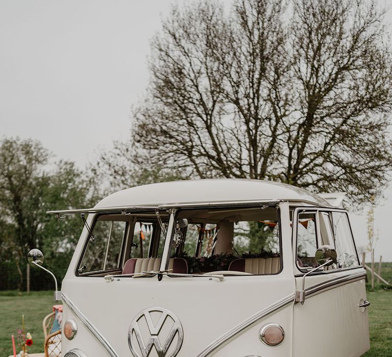 Cream VW vintage campervan wedding transport decorated with colourful flowers on the bumper 