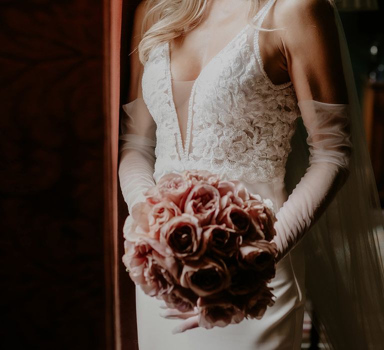 Pink rose round bouquet held by bride with sheer long gloves and v-neck wedding dress 