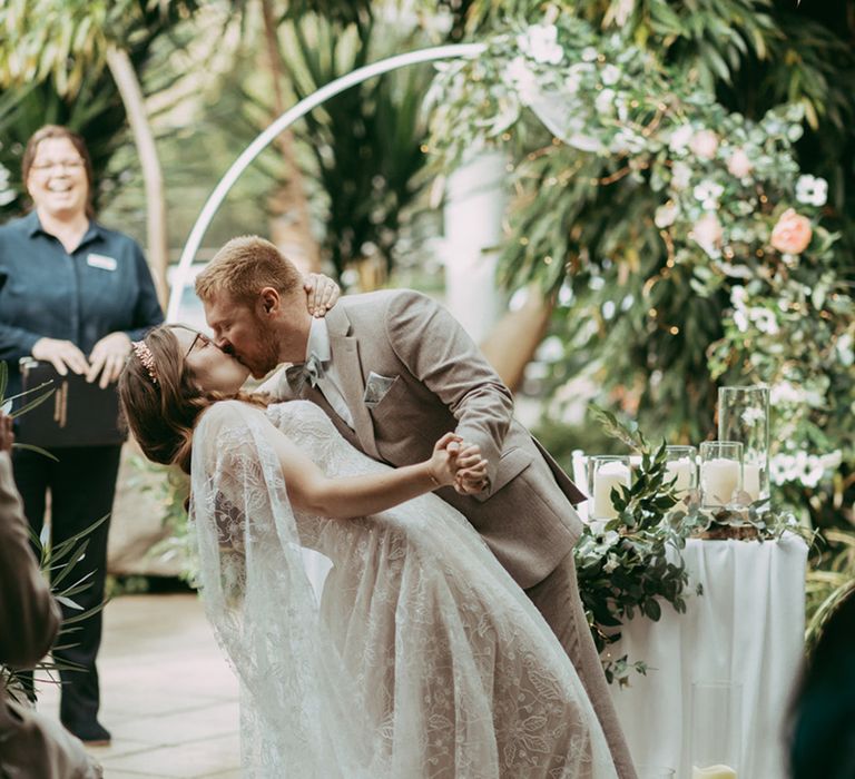 First kiss for the bride and groom at their wedding ceremony with a floral arch and sweetheart table decoration 