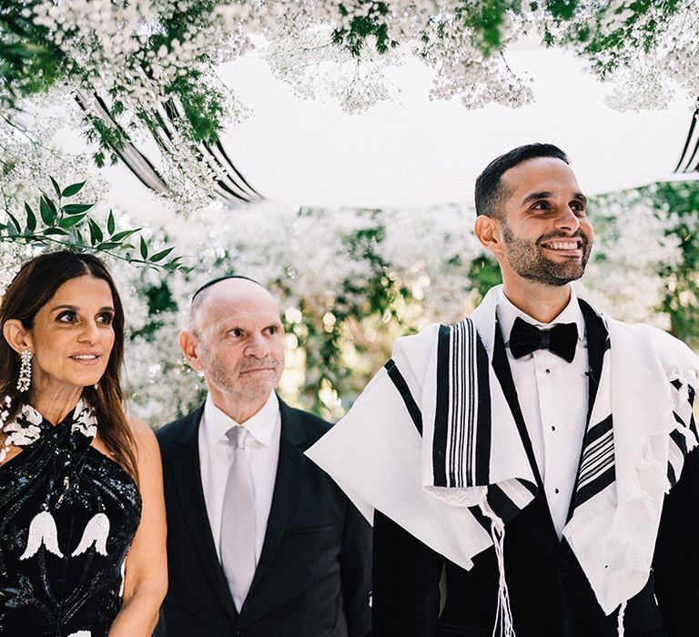 Groom in black tuxedo with tallit for Jewish prayers at the ceremony 