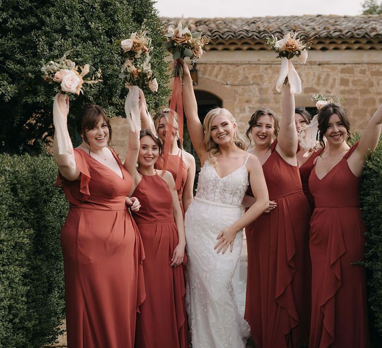 Bridal party wearing terracotta bridesmaid dresses carrying a neutral wedding bouquet 