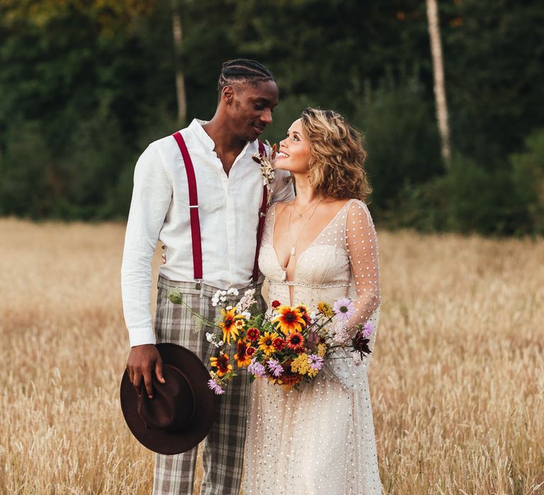 Bride & groom smile at one another in fields at Longton Wood