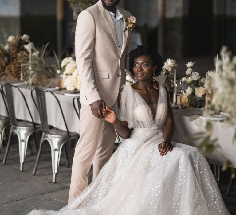 Bride and groom sitting at the wedding reception table holding hands 