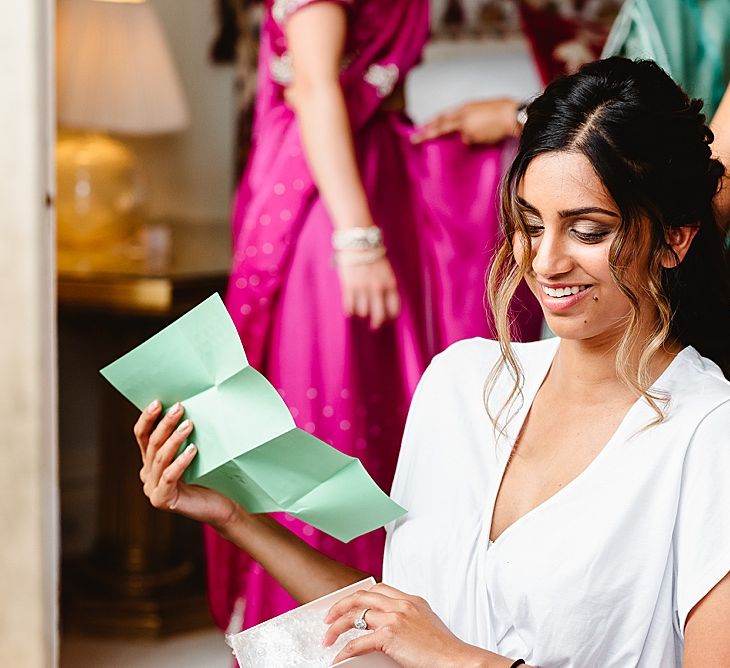 Beautiful Asian bride with half up half down wedding hair reading a note from the groom on the wedding morning 