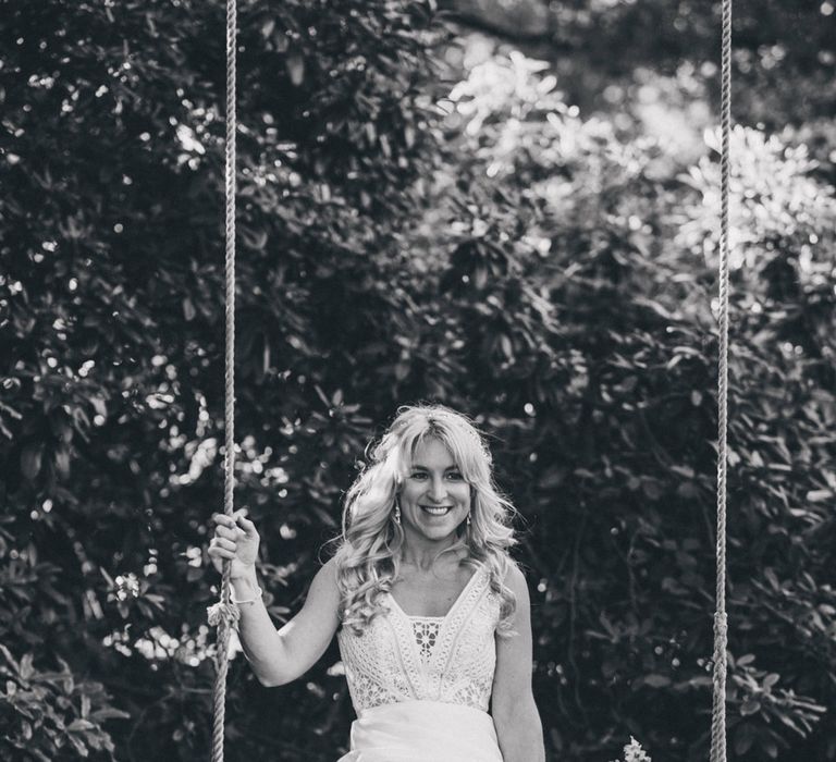 Smiling bride in Justin Alexander wedding dress sits on swing in the grounds at Iscoyd park wedding reception 