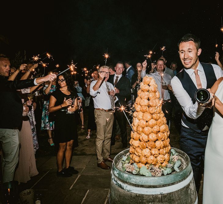 Croquembouche on top of barrel as couple and guests celebrate with sparklers