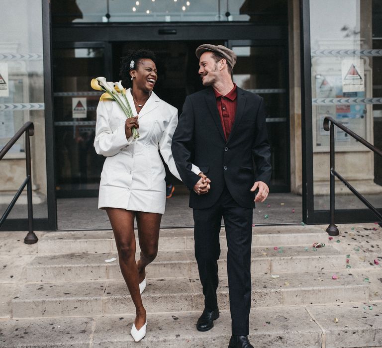 Bride and groom exiting their town hall wedding in a short wedding dress and flat cap 