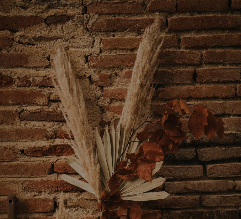 Apothecary jar filled with pampas grass, dried palm leaves and brown foliage 