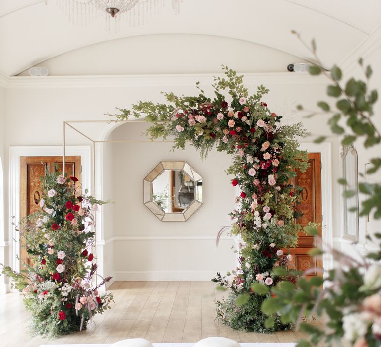 Floral archway in neutral wedding venue filled with green foliage and red florals