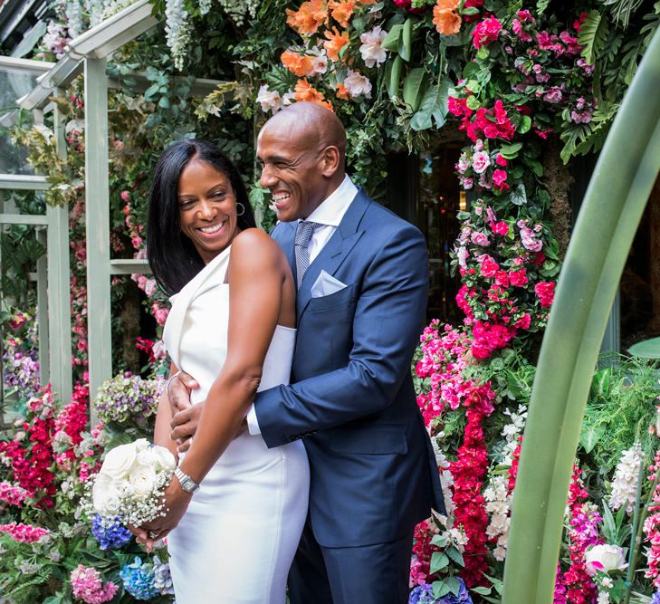 Bride in a fitted Roland Mouret dress standing outside a flower shop in Chelsea with her husband in a navy suit