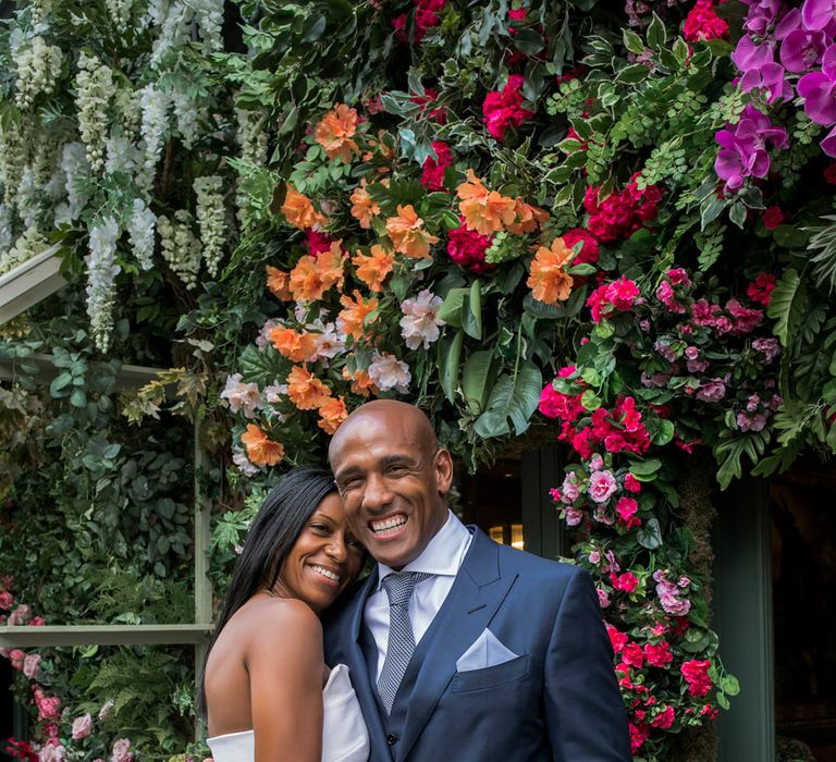 Stylish bride in a one shoulder Roland Mouret dress smiling with her groom in a navy three-piece suit in Chelsea