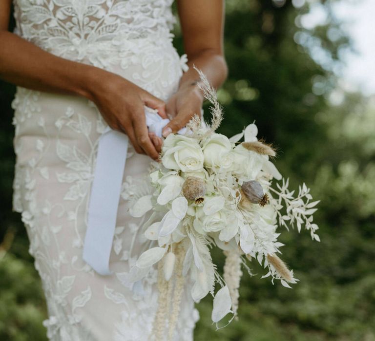 Boho bride holding bouquet of dried poppy heads, white roses, white flowers and white leaves