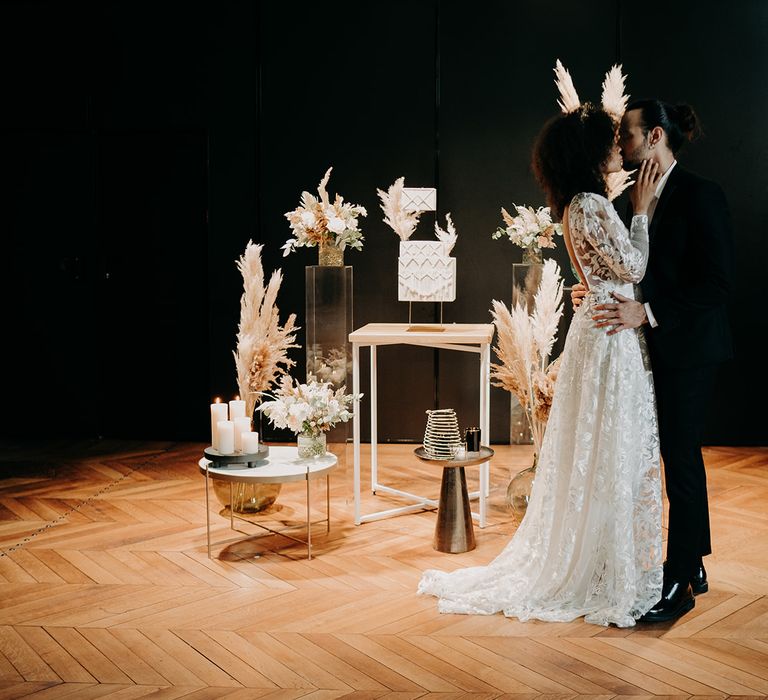 Bride & groom kiss in front of wedding cake stand