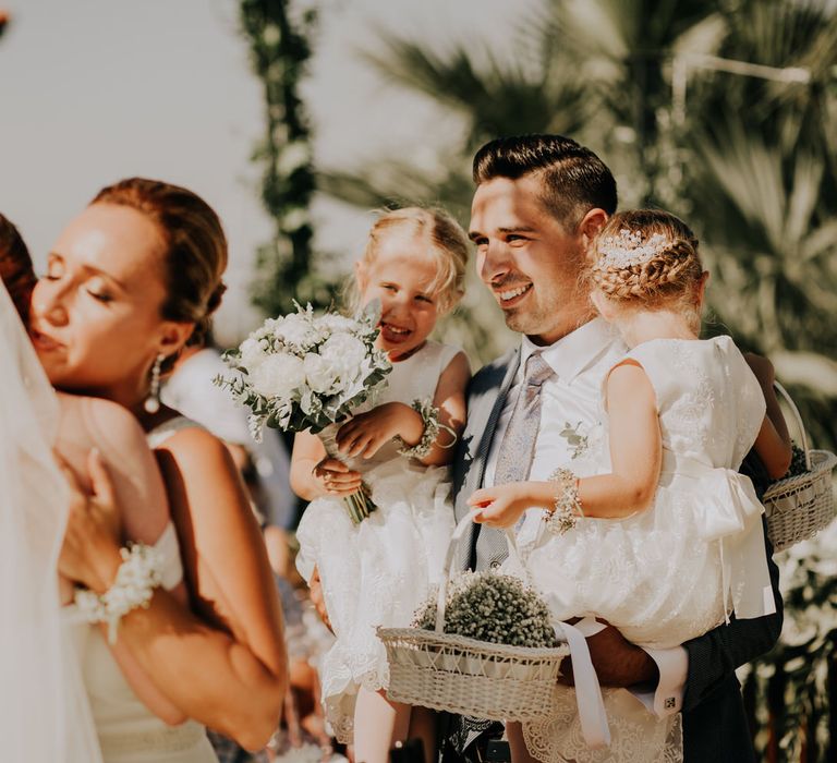 Bride hugging a guest as the groom holds two flower girls in his arms