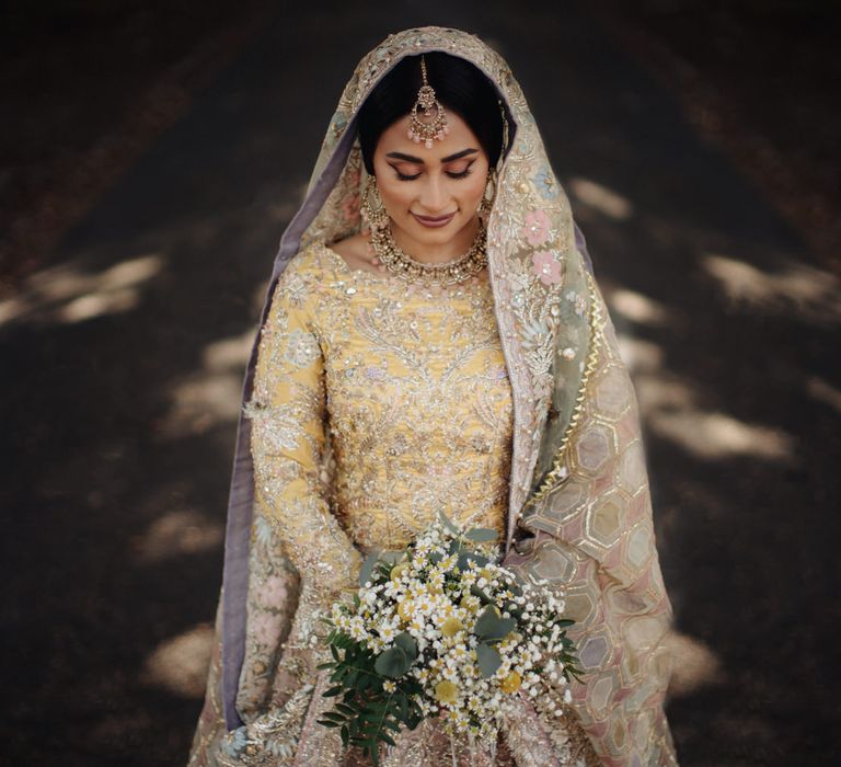 Indian bride in a pastel yellow, pink and mint Bengali wedding dress with gold thread design