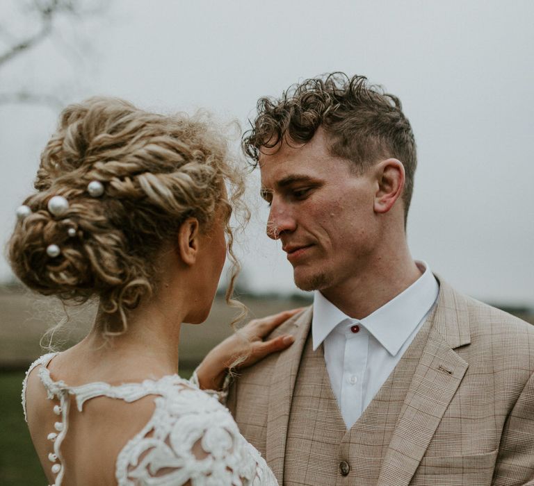 Bride with curly wedding hair in an up-do with pearl hair accessories, groom wearing a beige wedding suit